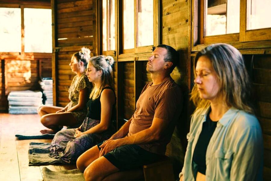 Group meditation session with the group seated against a wooden wall