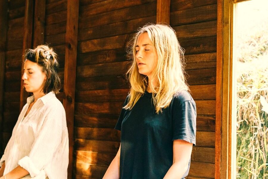 Two guests meditating with eyes closed in warm window light