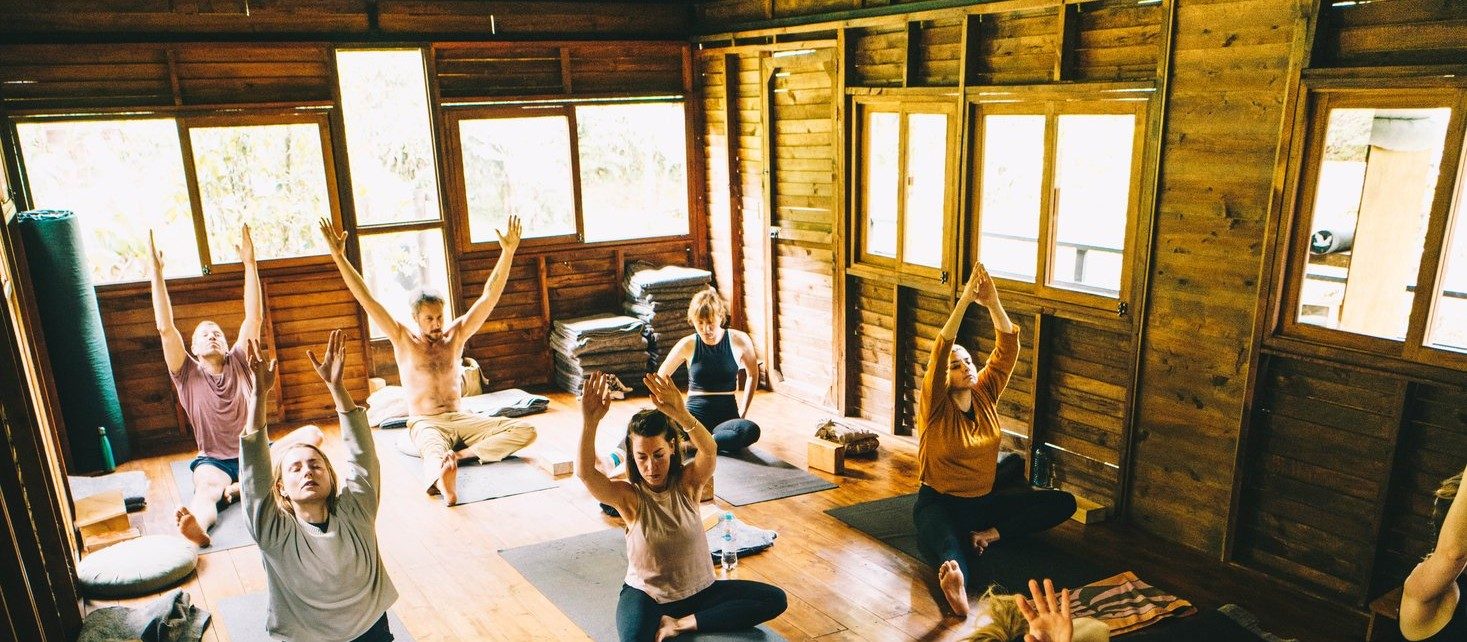 Clase grupal de yoga con los brazos hacia arriba en la shala